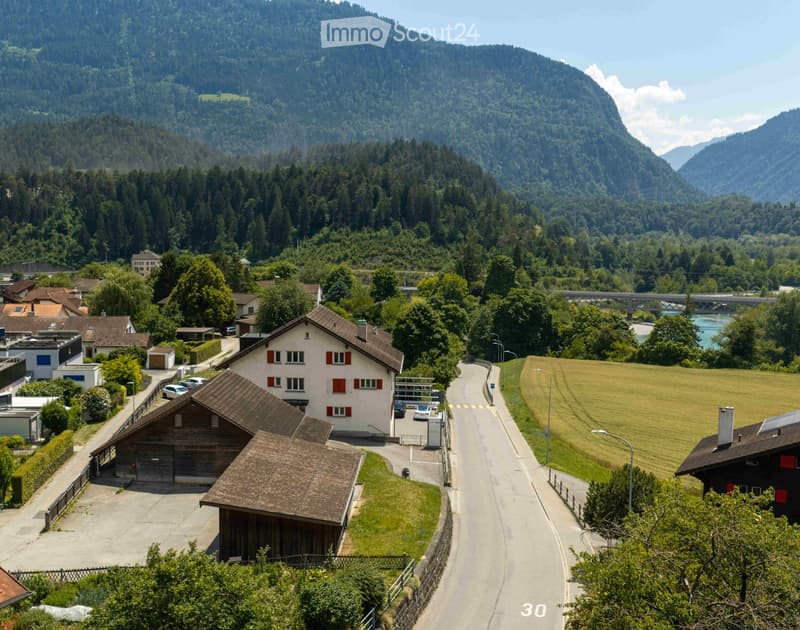 A scenic view of a village nestled in a valley with houses, a road, and surrounding mountains.
