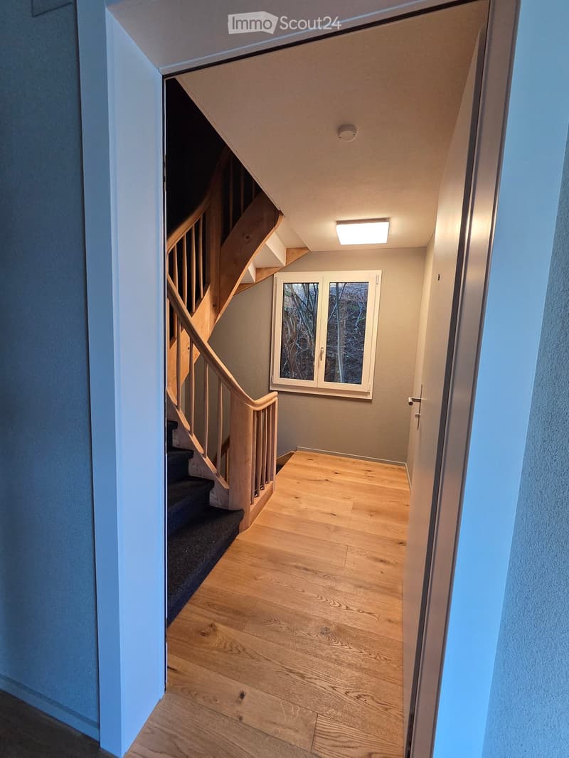 Spacious hallway with wooden flooring, a staircase with wooden railings, and a window with frosted glass panels.