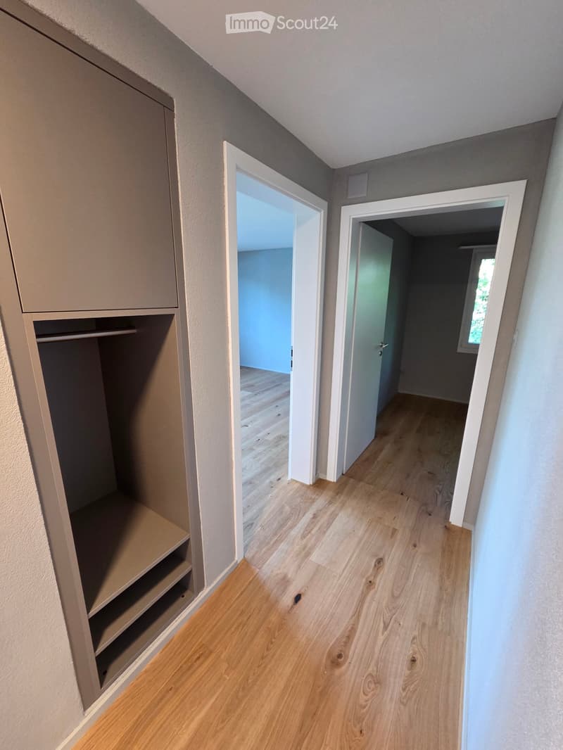 Empty hallway with light wooden flooring, built-in closet on one side, and two open doors leading to other rooms.