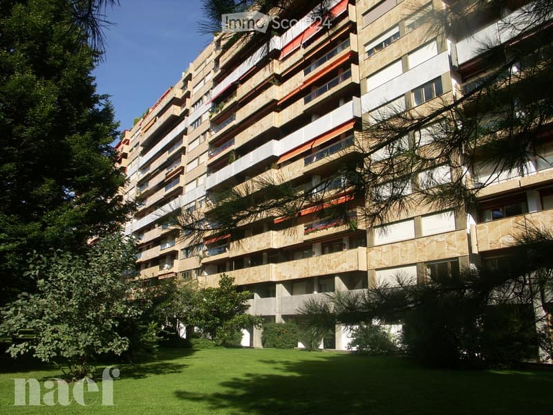A multi-story residential building with balconies and greenery in the foreground.