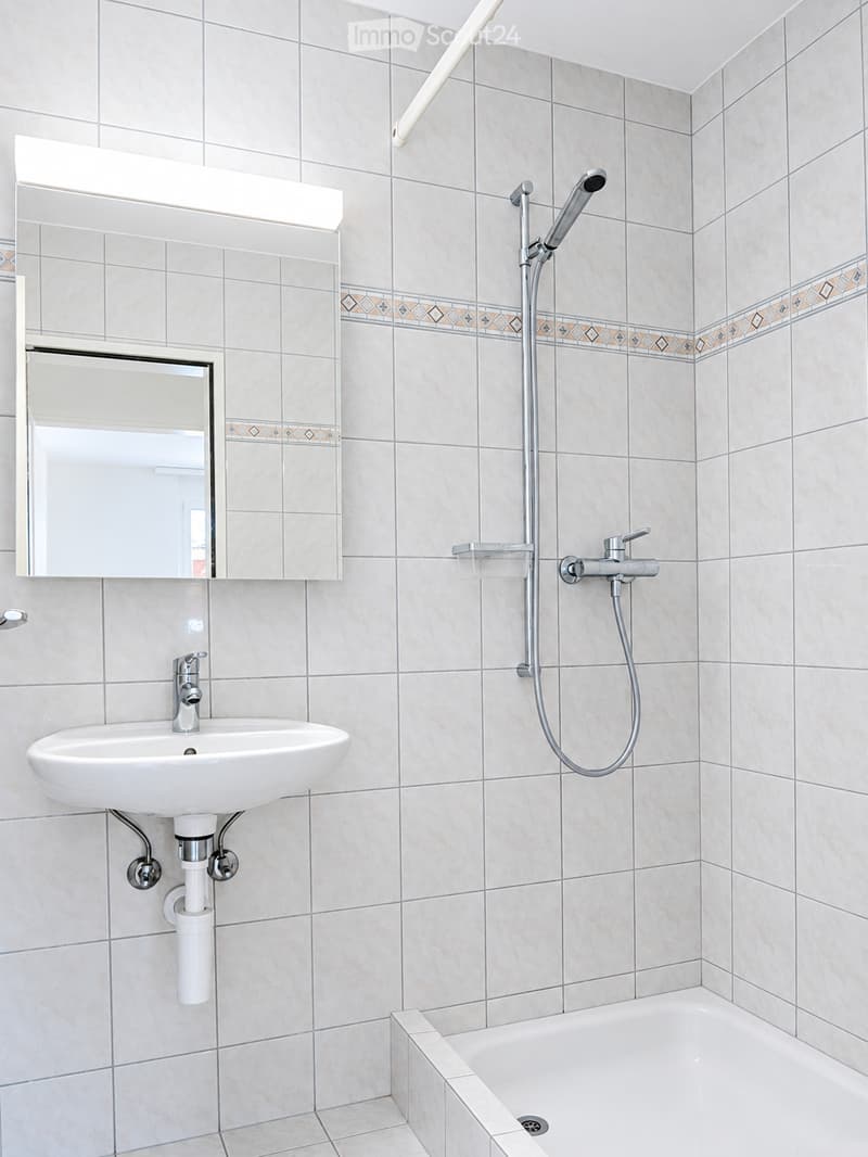 Modern bathroom with beige tiled walls, a white sink with a chrome faucet, a bathtub, a showerhead with a handheld sprayer, and a large mirror with built-in lighting.