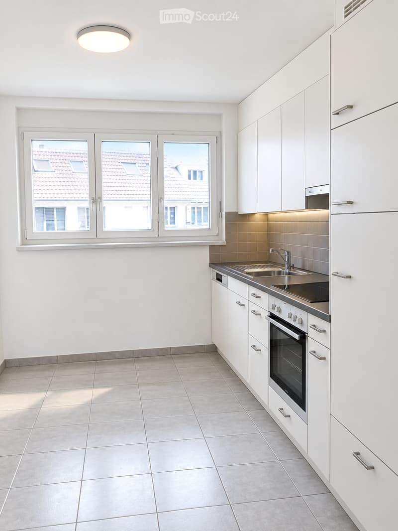 Modern kitchen with white cabinets, stainless steel appliances, tiled floor, and large windows overlooking a tiled roof.