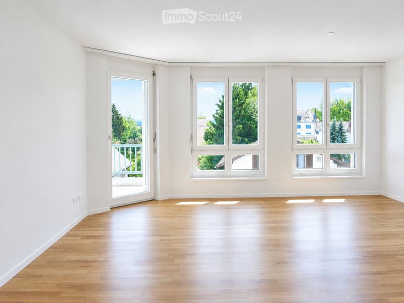 Empty room with light wooden flooring, white walls, and multiple windows including a sliding glass door leading to a balcony.