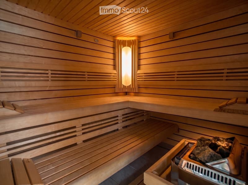 A wooden sauna with multiple benches, a light fixture, and a stone rock pile in the corner.