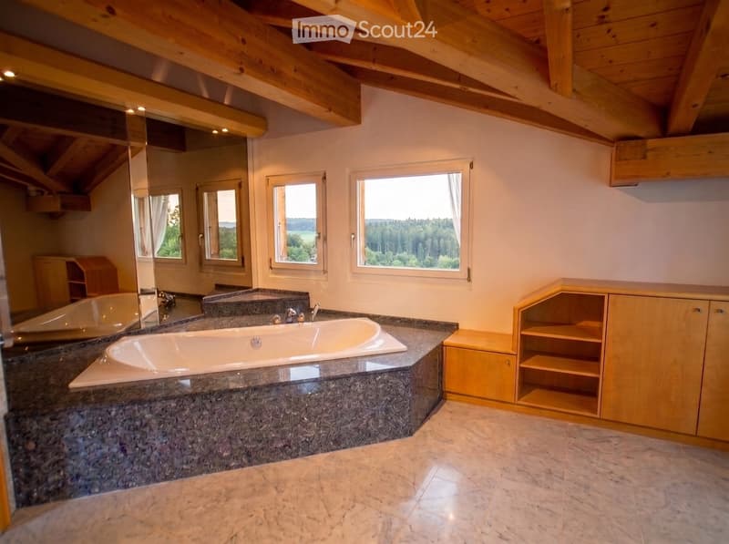 Spacious bathroom with a large bathtub, marble countertops, wooden cabinets, and large windows offering a scenic view.