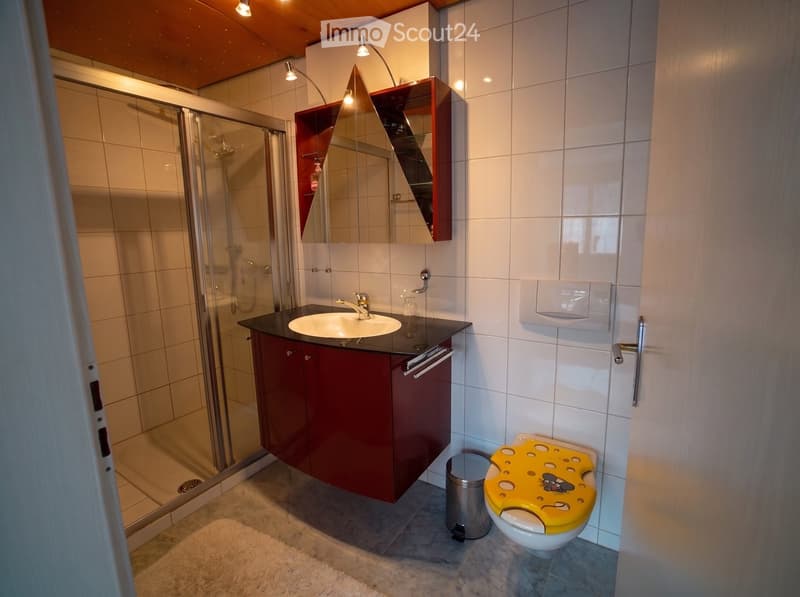 Modern bathroom with a red cabinet, white tiles, a black countertop, a sink, a mirror, a shower, and a toilet with a yellow seat cover.
