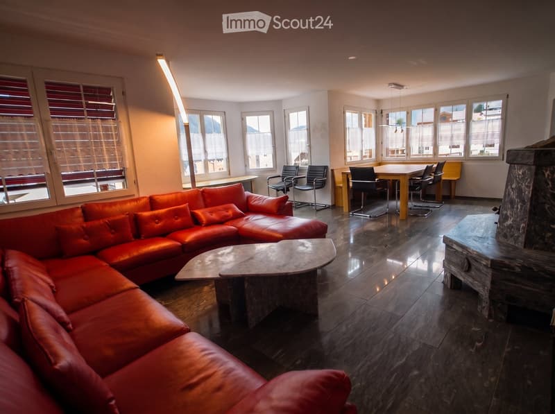 Modern living room with a red leather sectional sofa, coffee table, fireplace, dining area with table and chairs, large windows with blinds, and a tall floor lamp.