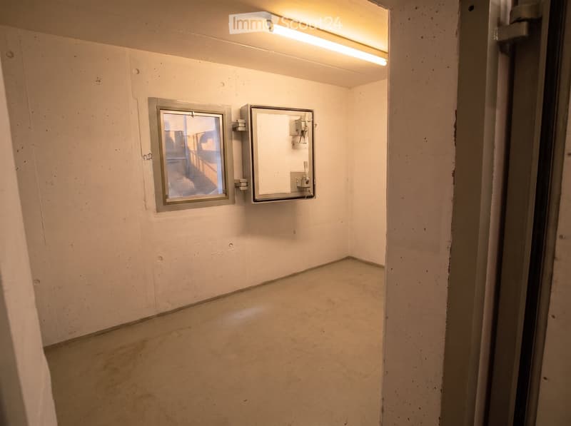 Empty room with white walls, concrete floor, small window, and a mirror on the wall.