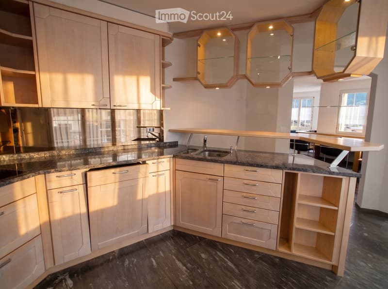 Modern kitchen with light wood cabinets, granite countertops, stainless steel sink, and built-in mirrors above the sink area.