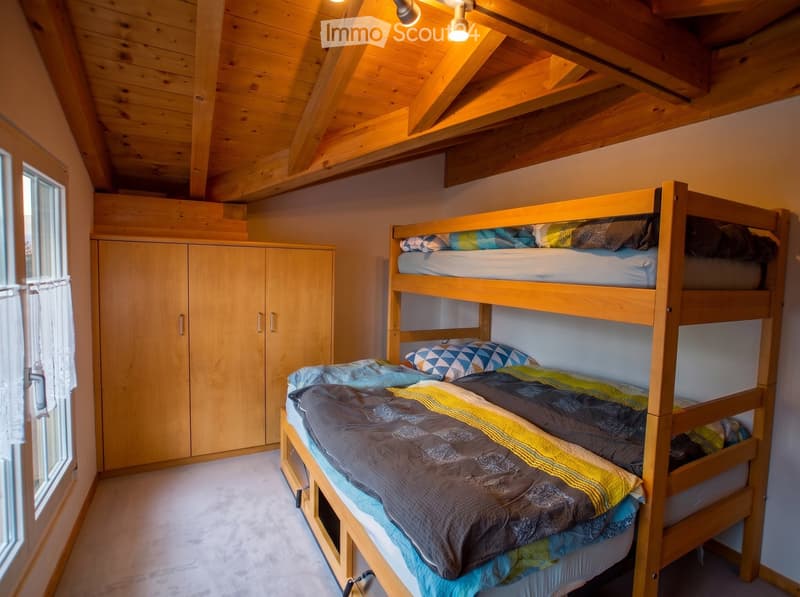 Cozy bedroom with a wooden bunk bed, neatly made with colorful bedding, and a matching wooden wardrobe.