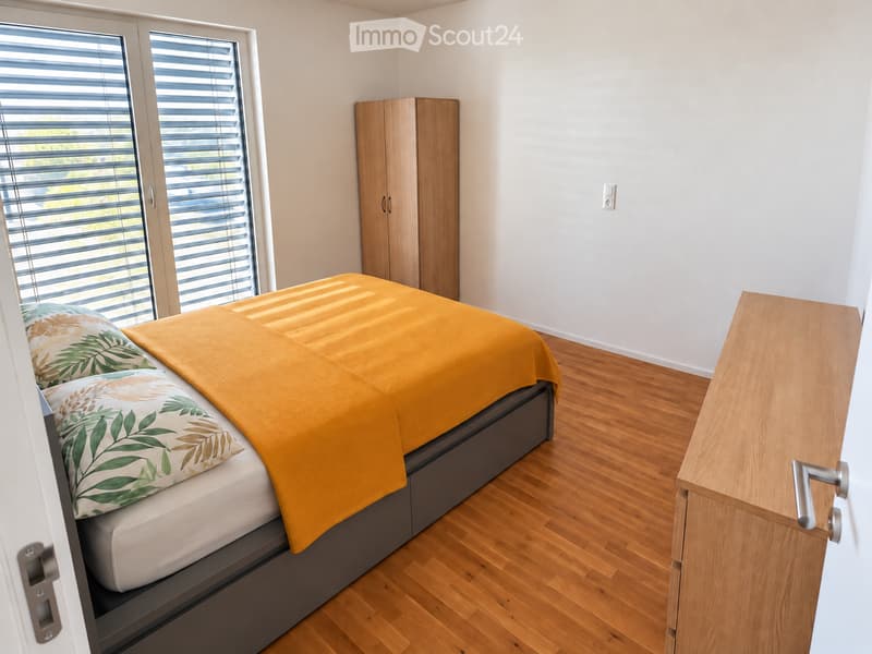 Modern bedroom with a wooden bed, orange blanket, decorative pillows, a wardrobe, and a desk with a drawer.