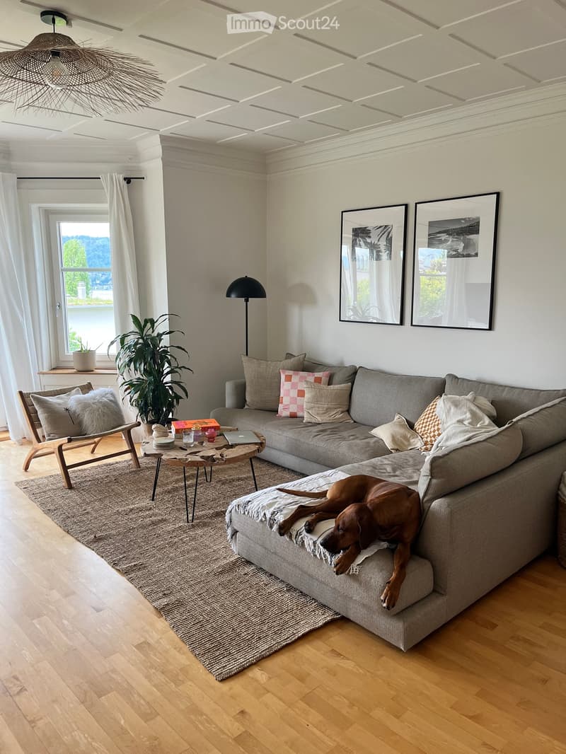 Modern living room with grey sectional sofa, wooden coffee table, floor lamp, and large window with view.
