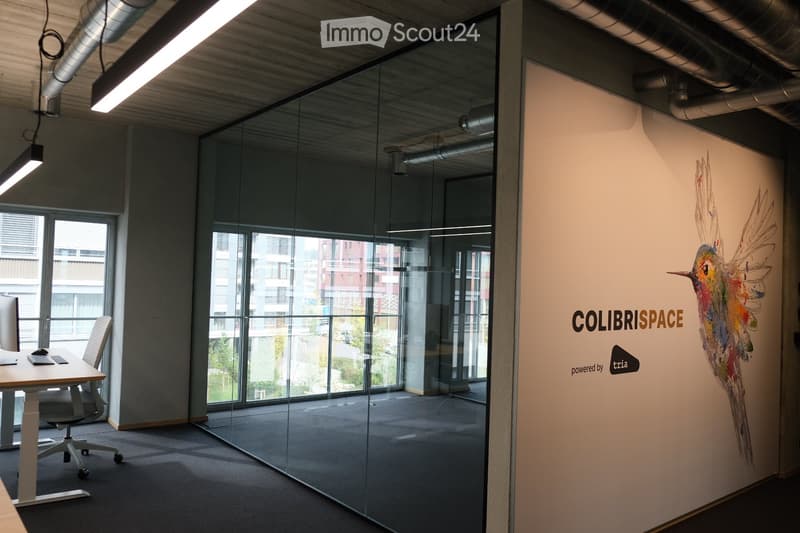 Modern office space with glass partitions, a desk with a computer setup, and a colorful mural on the wall.