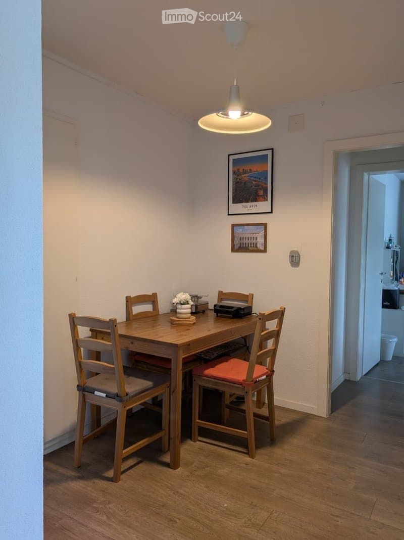 Dining area with wooden table, four chairs, flower vase, and picture frames on the wall.