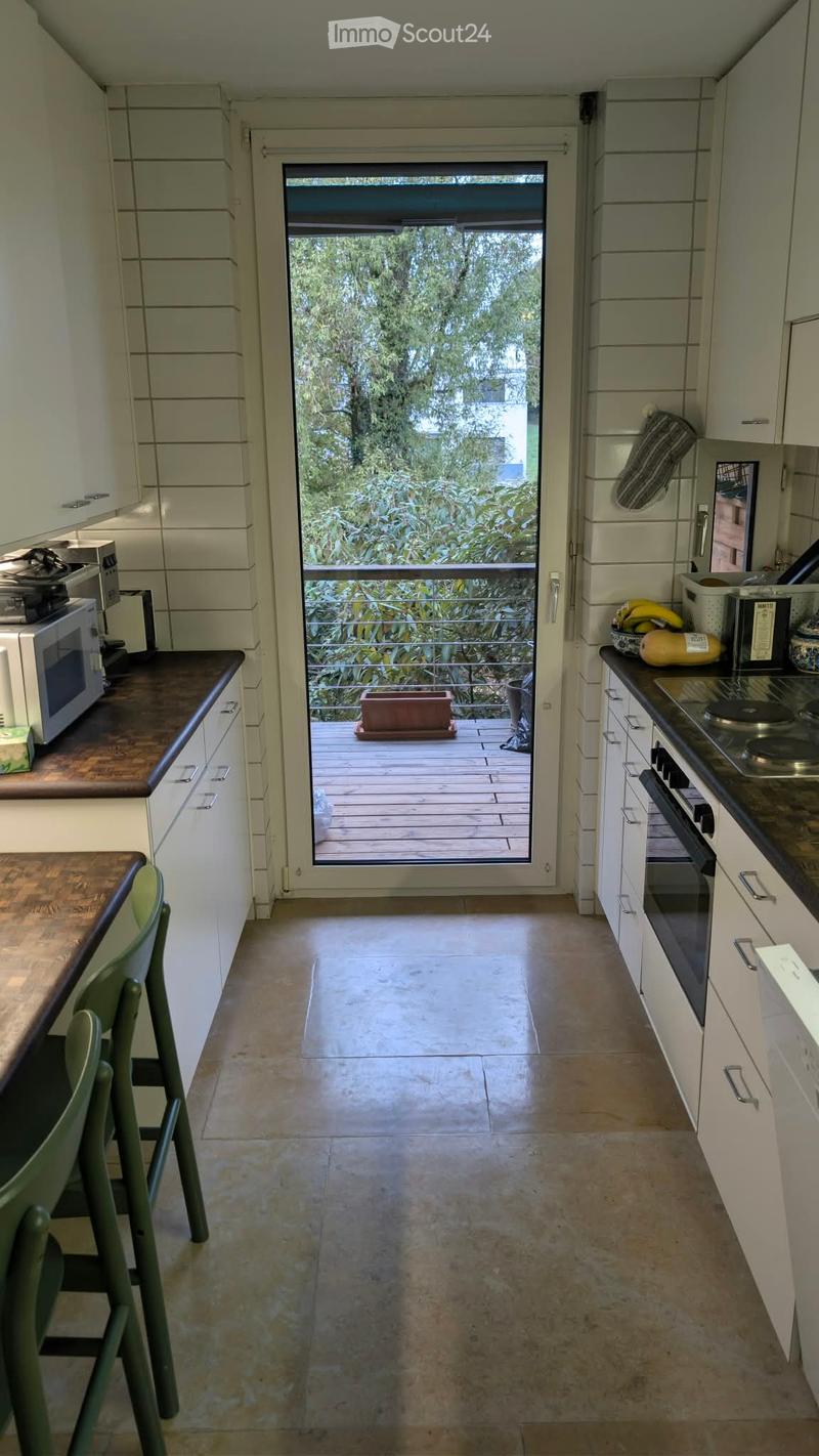 Modern kitchen with white cabinets, dark countertops, and a sliding glass door leading to a balcony. Includes a microwave, oven, and a chair near the counter.