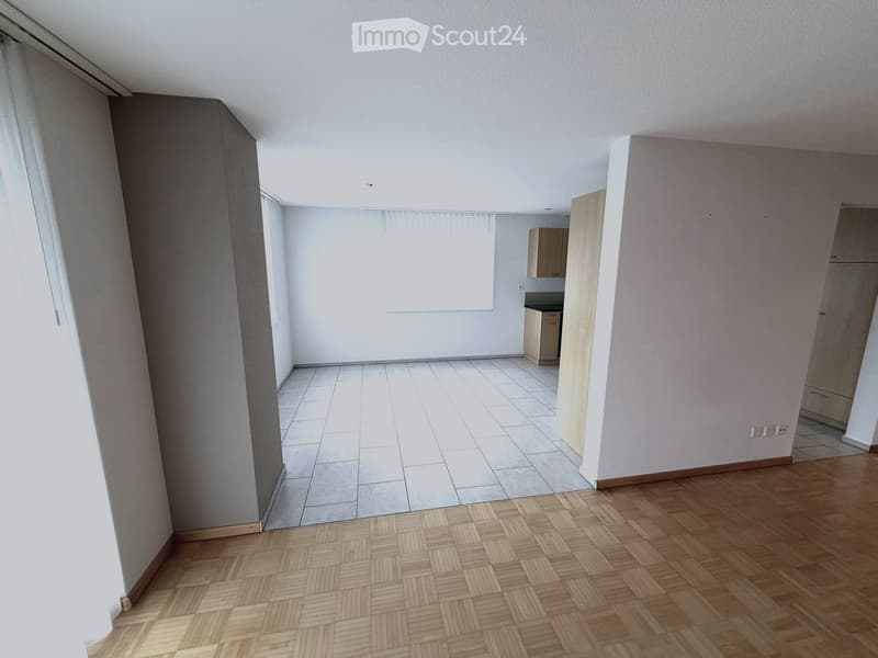 Empty room with wooden flooring and tiled section, white walls, and large windows with blinds. No furniture or equipment present.