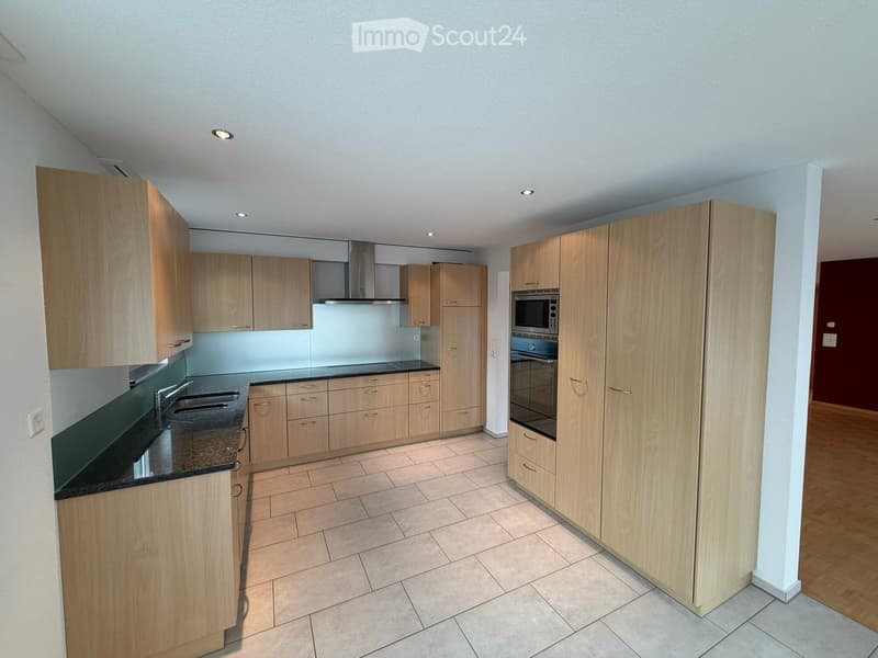 Modern kitchen with light wooden cabinets, black countertop, stainless steel sink, microwave, and oven.
