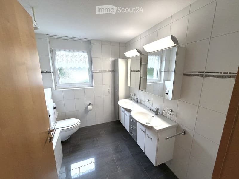 Modern bathroom with white tiles, a double sink vanity, a toilet, and a large mirror with built-in lighting.