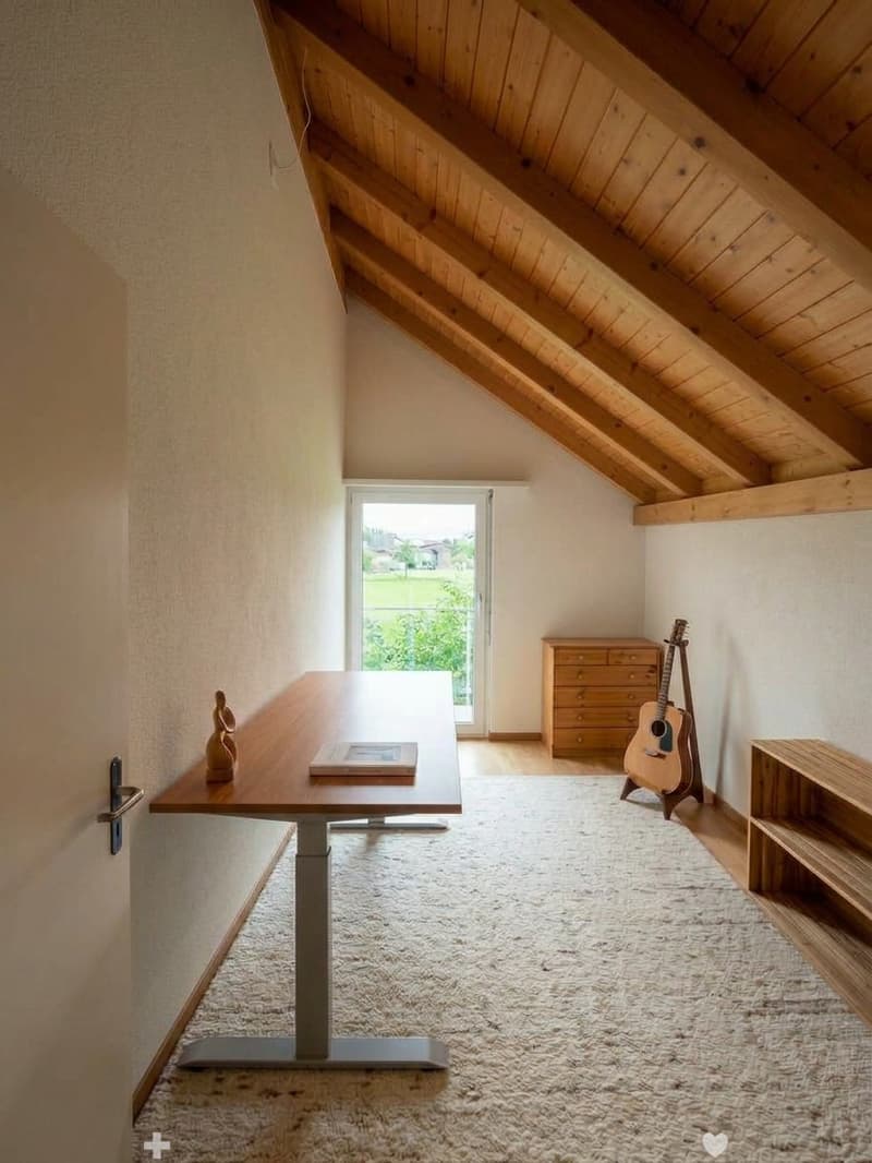 Bright attic room with wooden beams, large window, carpeted floor, modern table, guitar, and wooden shelves.