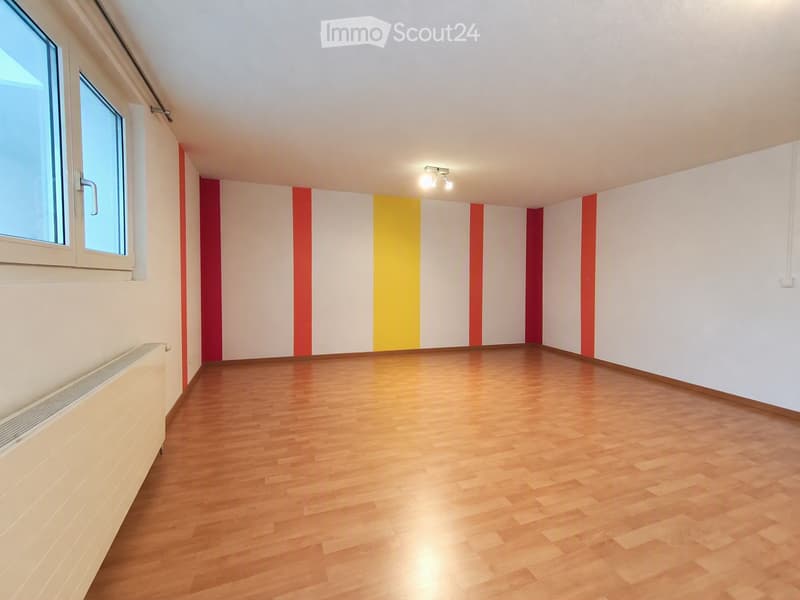 Empty room with wooden flooring, white walls with red and yellow stripes, and a window with white frame. No furniture or equipment present.