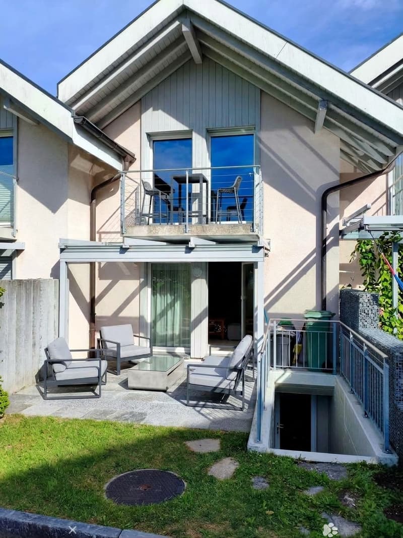 Modern outdoor space with a raised patio, lounge chairs, coffee table, and a small balcony with outdoor furniture.