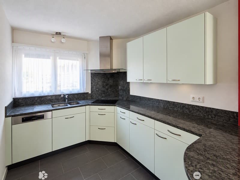 Modern kitchen with white cabinets, granite countertops, stainless steel sink, dishwasher, and range hood. Features a window with white blinds and built-in lighting.