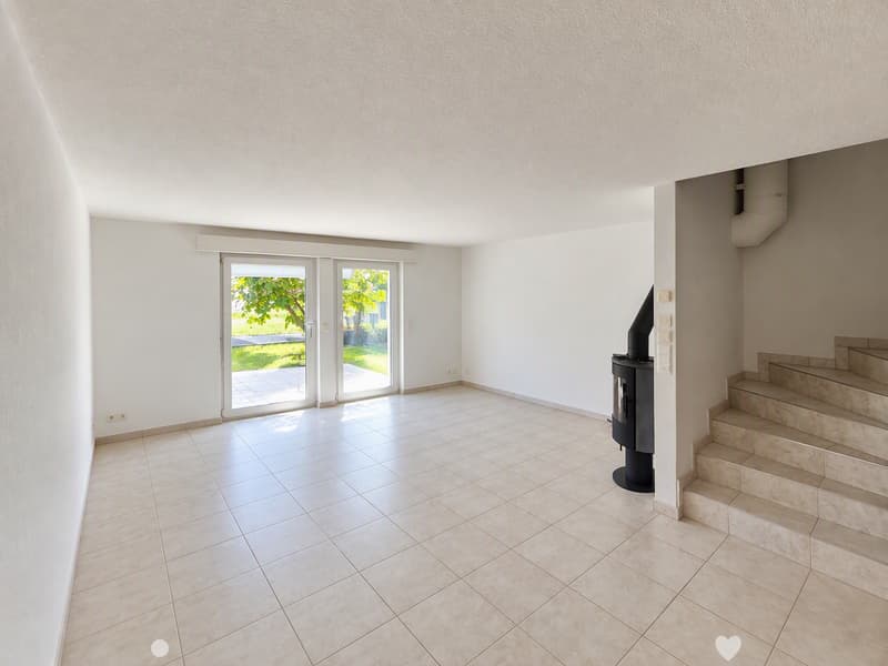 Empty room with tiled floor, white walls, large glass doors leading to a garden, and a staircase leading upwards.
