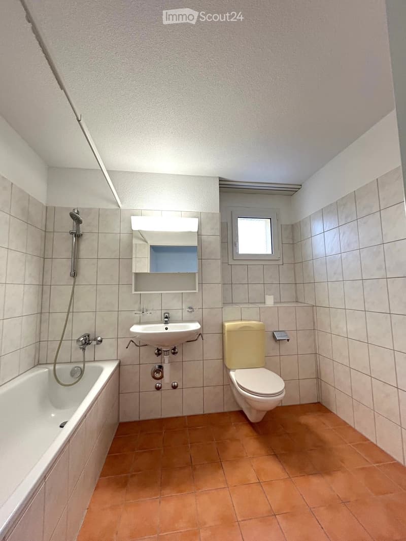 Bathroom with tiled walls, a bathtub, toilet, sink, mirror, and a small window.
