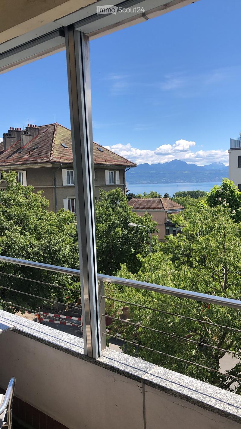 Balcony with metal railing, overlooking a scenic view of a lake, mountains, and surrounding buildings.