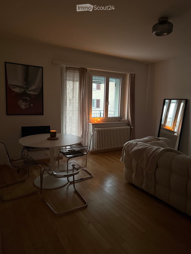 Living room with wooden floor, sofa, round table, chairs, mirror, and picture frame on the wall.