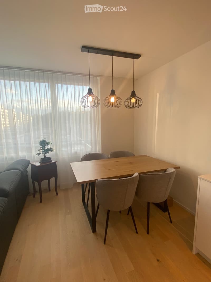 Dining area with a wooden dining table, six chairs, pendant lights, a small side table with a bonsai tree, and a blue sofa visible in the background.