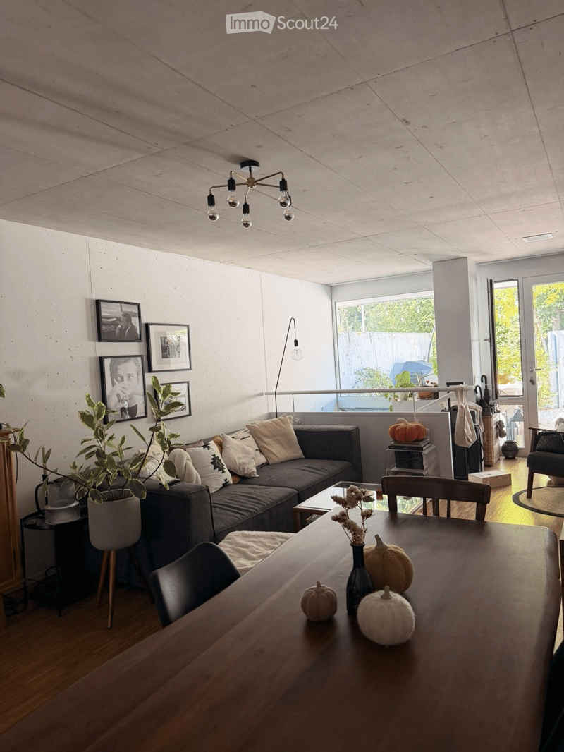 Living room with a grey sectional sofa, coffee table, dining table with chairs, decorative pumpkins, potted plant, picture frames, and a floor lamp.