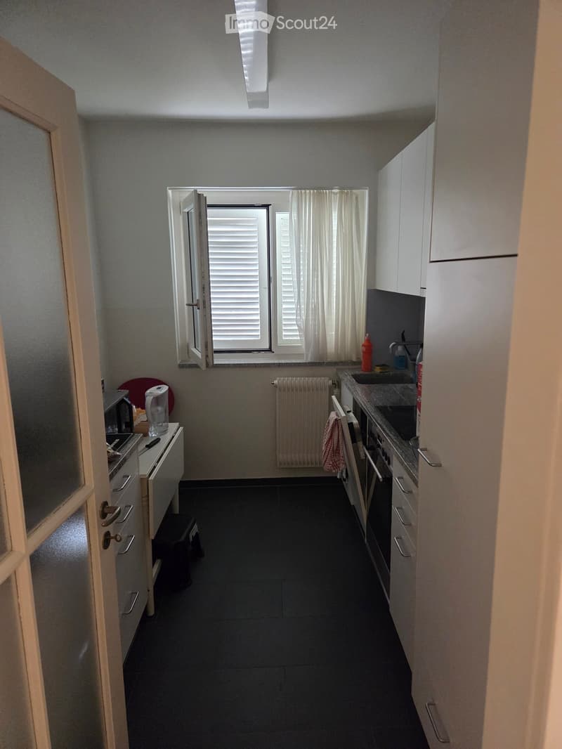 Modern kitchen with white cabinets, dark tiled floor, microwave, fridge, oven, sink, and window with white curtains.