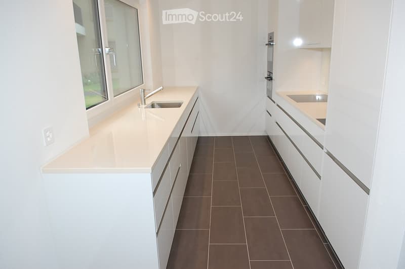 Modern kitchen with white cabinets, beige countertops, and a brown tiled floor. Features a sink with a modern faucet and built-in cabinets.