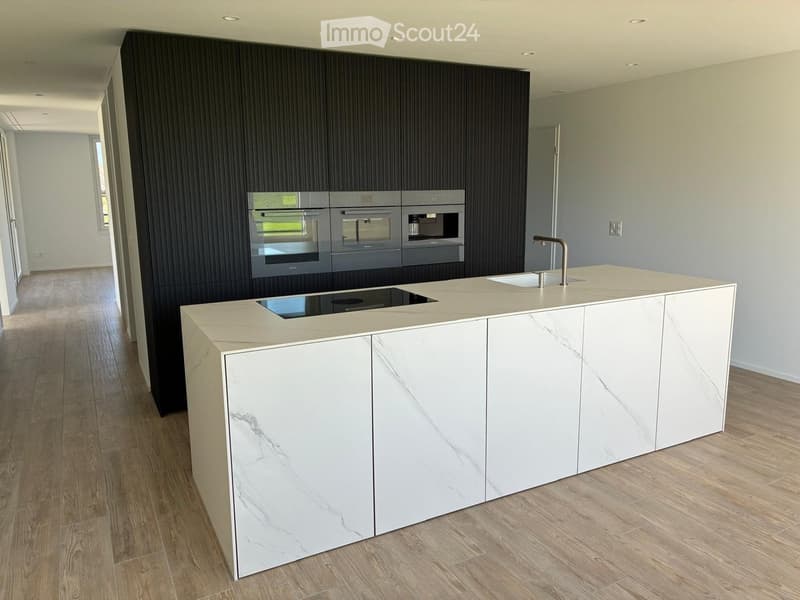 Modern kitchen with a white marble island, built-in ovens, and a sleek faucet.