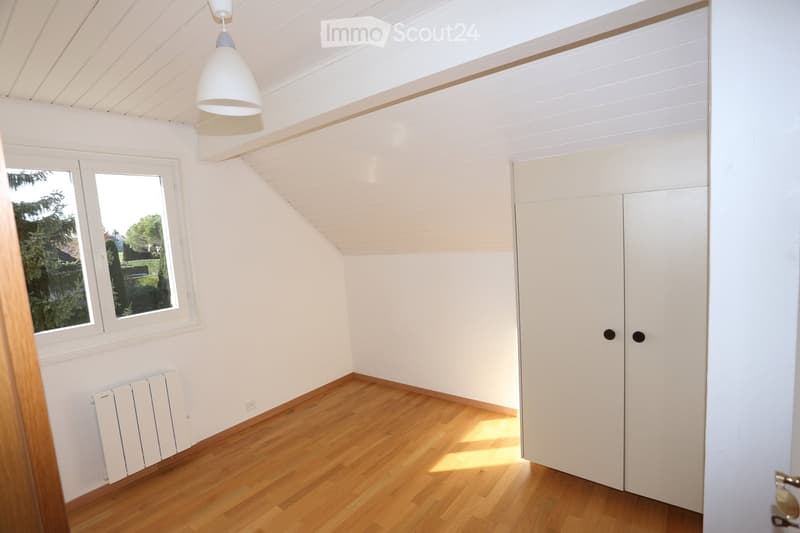 Bright, empty room with wooden flooring, white walls, and a large window offering a view of greenery. Features a built-in wardrobe and a radiator under the window.