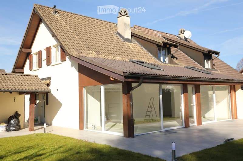 Two-story house with a tiled roof, white and brown exterior, large glass sliding doors leading to a patio, chimney, satellite dish, and a small covered porch area.