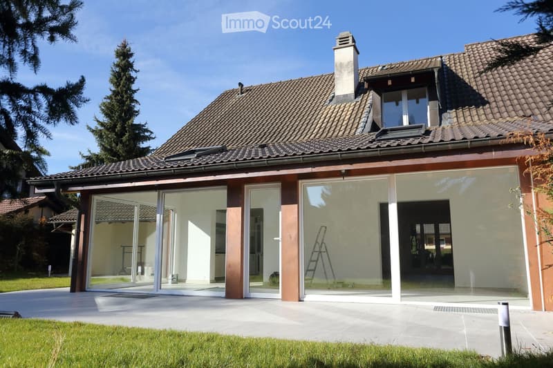 Two-story house with a tiled roof, large glass sliding doors, and a well-maintained lawn.