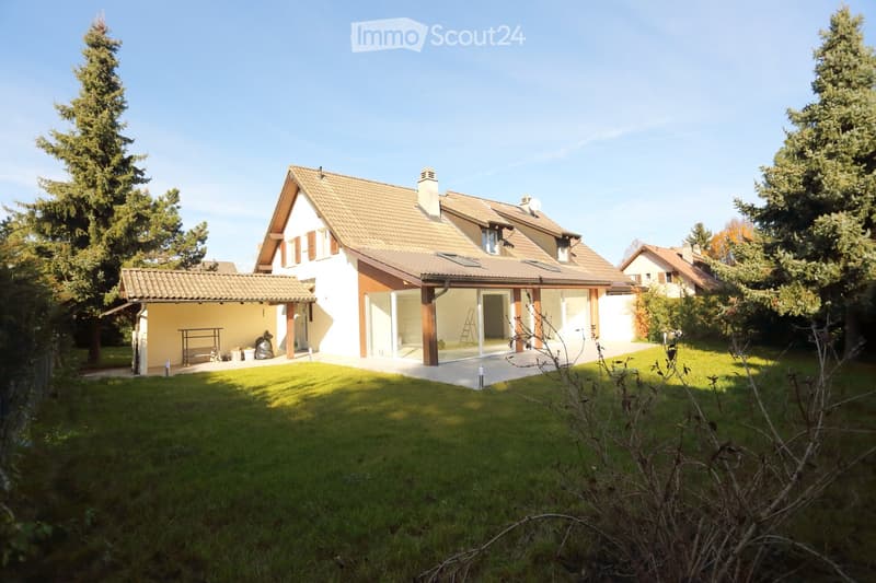 Two-story house with a tiled roof, white walls, and a covered patio area. The house features large windows and a modern design, surrounded by a well-maintained lawn and trees.