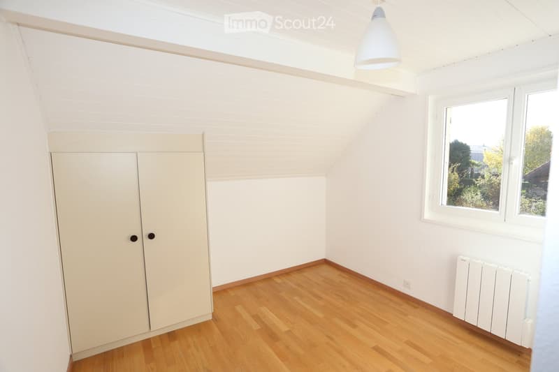 Empty room with wooden flooring, white walls, a built-in closet, and a window offering a view of greenery outside.