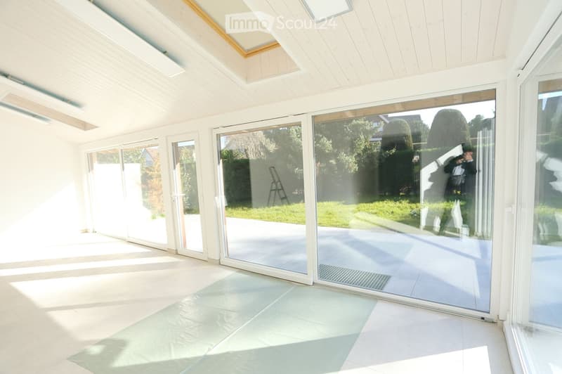 Bright, open room with large glass sliding doors leading to an outdoor area, white walls, and a light-colored tiled floor.