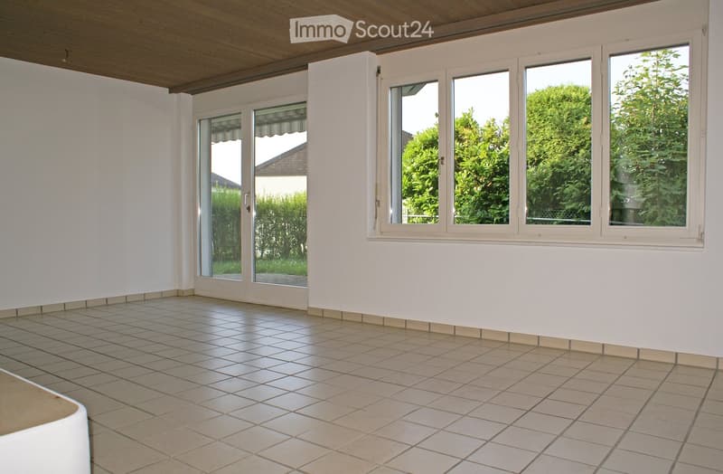 Empty room with tiled floor, white walls, large windows, and a wooden ceiling.