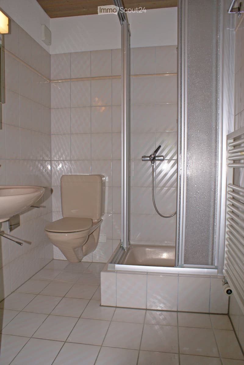 A small bathroom with beige tiles, a toilet, a sink, and a shower with a glass enclosure.