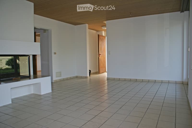 Empty hallway with tiled floor, white walls, and a fireplace on the left side. The hallway leads to another room with a wooden door.