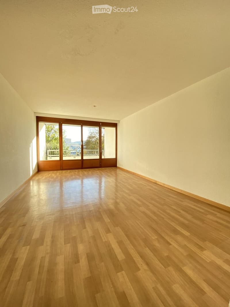 Empty room with light wooden flooring and large sliding glass doors leading to a balcony or outdoor area.