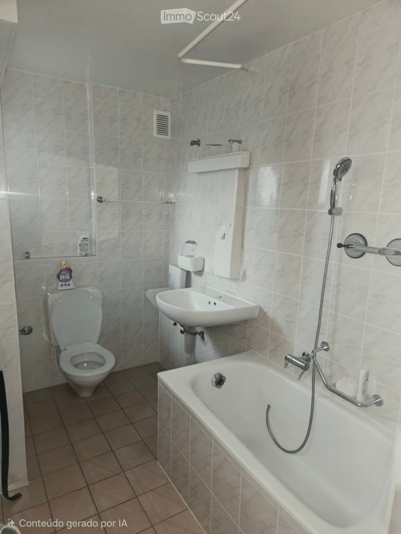 Modern bathroom with beige tiles, a toilet, a sink, a bathtub with a handheld shower, and a grab bar for safety.