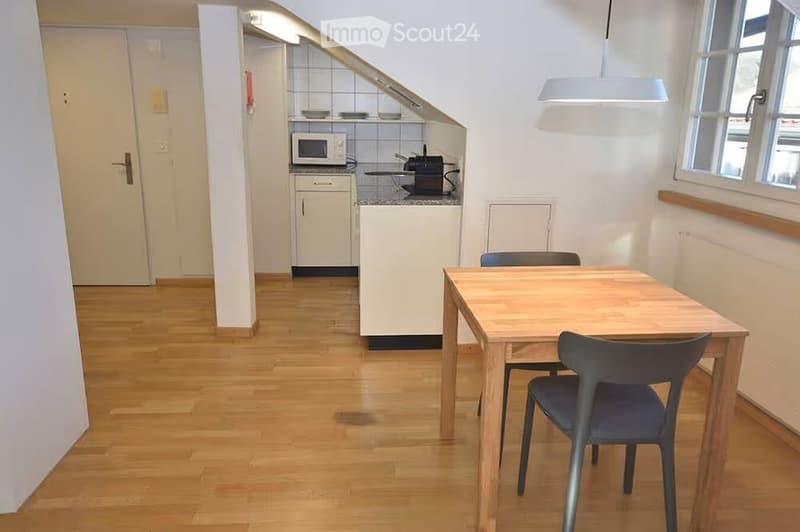 A compact, modern kitchen and dining area with light wooden flooring, white cabinets, a microwave, and a small dining table with chairs.