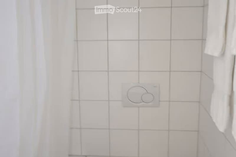 White tiled wall in a bathroom with a visible electrical outlet featuring two circular symbols.