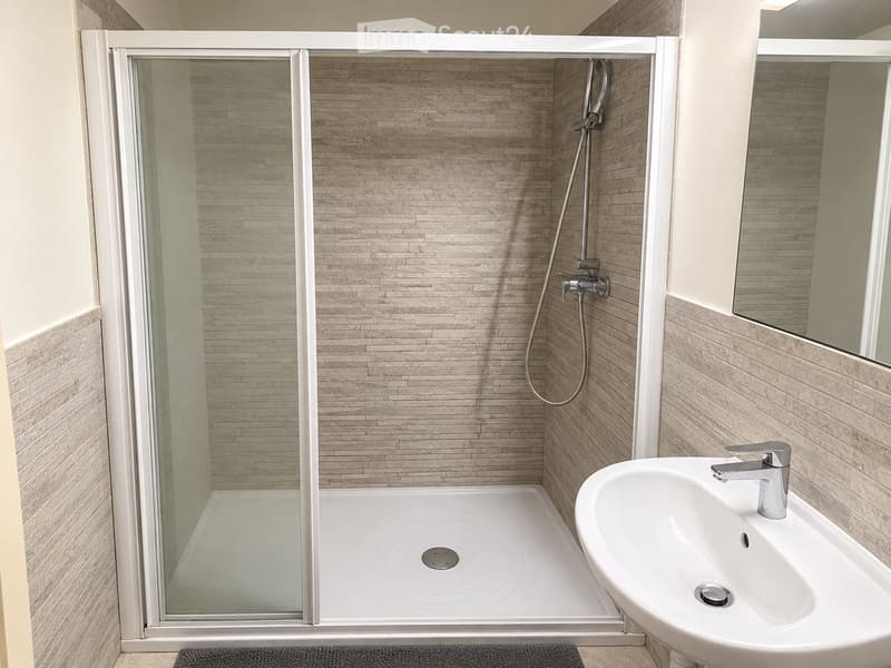 Modern bathroom with a glass-enclosed shower, a white sink with a chrome faucet, and beige tiled walls.