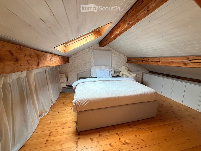 Cozy attic bedroom with wooden floors, slanted wooden ceiling, exposed stone wall, and built-in white cabinets.